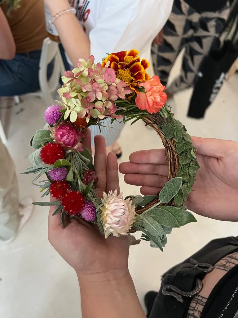 Two hands holding a finished wreath of strawflowers, hydrangea, sage, and a marigold.